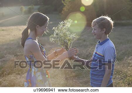 Boy giving girl flowers in field View Large Photo Image Stock Image - Boy giving girl flowers in field. Fotosearch