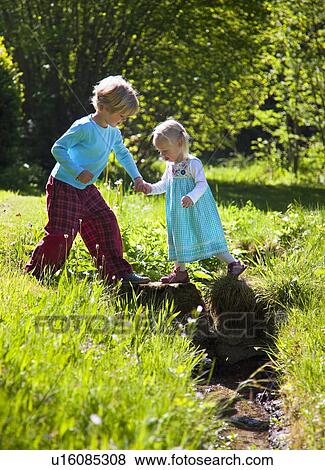 Stock Photo - Boy helping sister cross creek. Fotosearch