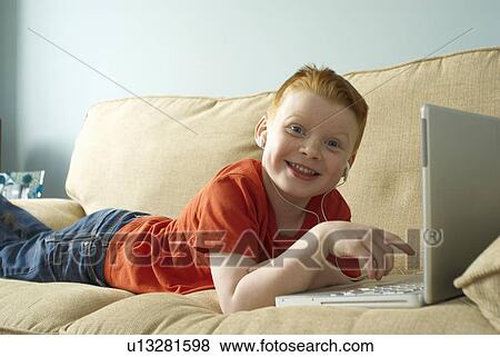Boy in headphones using laptop on couch View Large Photo Image Stock Photo - Boy in headphones using laptop on couch. Fotosearch