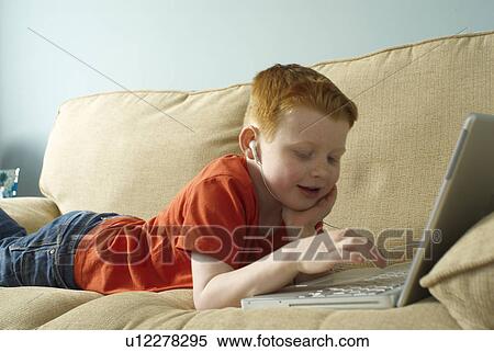 Boy in headphones using laptop on couch View Large Photo Image Stock Photography - Boy in headphones using laptop on couch. Fotosearch