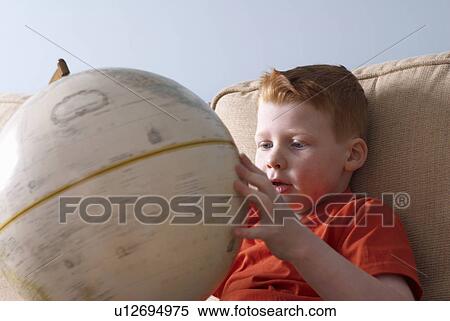 Stock Photography - Boy on couch examining globe. Fotosearch