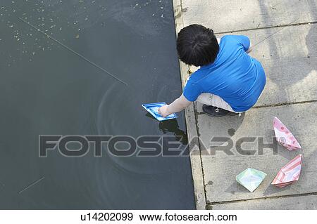 Boy playing with paper sailboats in pond View Large Photo Image Stock Photo - Boy playing with paper sailboats in pond. Fotosearch