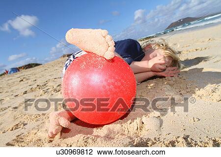 Stock Image - Boy playing with red ball on beach. Fotosearch
