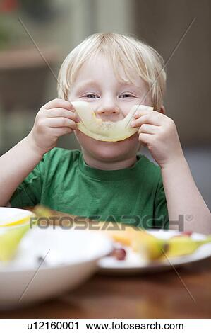 Stock Image - Boy playing with slice of melon at table. Fotosearch