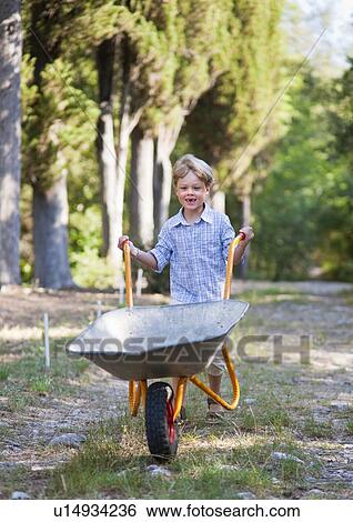 Boy pushing wheelbarrow outdoors View Large Photo Image Stock Photograph - Boy pushing wheelbarrow outdoors. Fotosearch