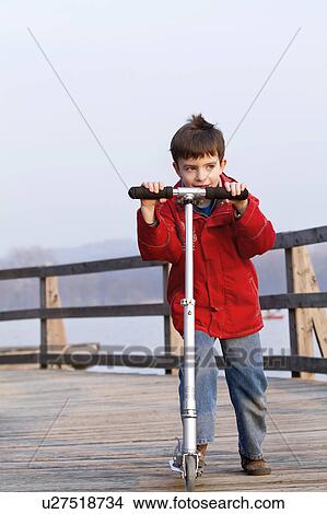 Picture - Boy riding scooter on dock over lake. Fotosearch