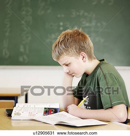 Stock Image - Boy studying at desk in classroom. Fotosearch