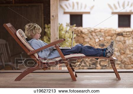 Boy using laptop in deck chair View Large Photo Image Stock Image - Boy using laptop in deck chair. Fotosearch