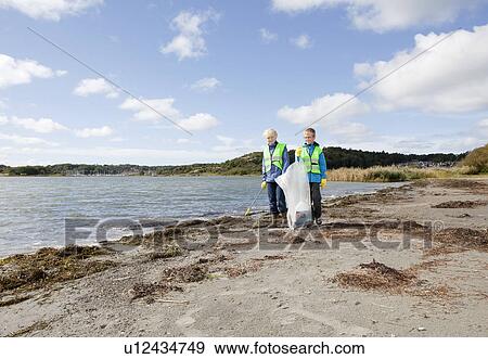 Stock Photo - Boys in safety vests cleaning beach. Fotosearch