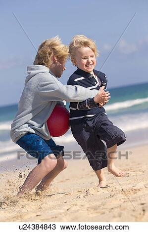 Stock Image - Boys playing with red ball on beach. Fotosearch