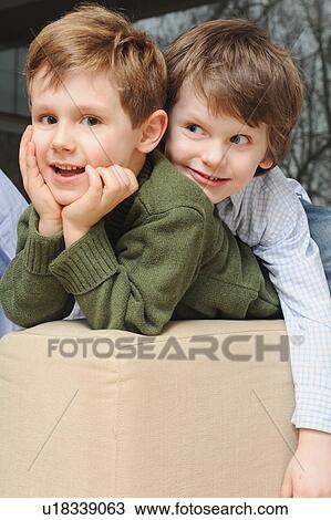 Stock Image - Boys sitting on sofa together. Fotosearch