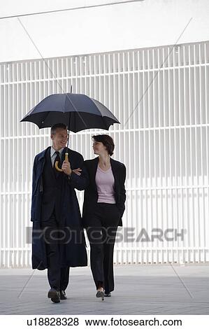 Stock Photo - Business people walking under umbrella. Fotosearch