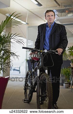 Stock Image - Businessman bringing bicycle into office. Fotosearch