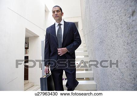 Stock Image - Businessman carrying briefcase on steps. Fotosearch