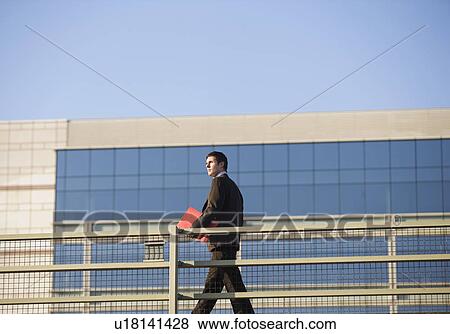 Businessman carrying folder on walkway View Large Photo Image Stock Photo - Businessman carrying folder on walkway. Fotosearch