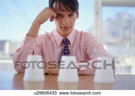Stock Image - Businessman examining cups in office. Fotosearch