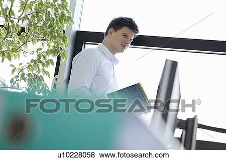 Stock Photo - Businessman holding book in office. Fotosearch