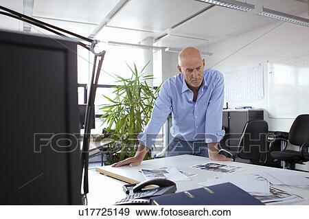 Businessman leaning over desk in office View Large Photo Image Stock Photo - Businessman leaning over desk in office. Fotosearch