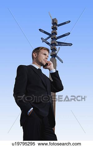 Stock Photography - Businessman on cell phone at crossroads. Fotosearch