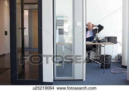 Businessman relaxing at desk in office View Large Photo Image Picture - Businessman relaxing at desk in office. Fotosearch