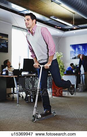Businessman riding scooter in office View Large Photo Image Stock Photo - Businessman riding scooter in office. Fotosearch