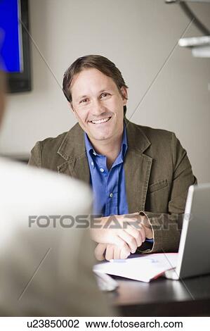 Businessman smiling at desk in office View Large Photo Image Stock Image - Businessman smiling at desk in office. Fotosearch