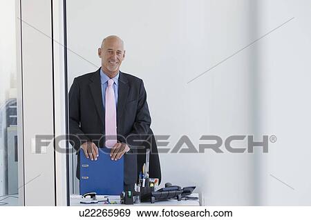 Businessman standing at desk in office View Large Photo Image Stock Photo - Businessman standing at desk in office. Fotosearch