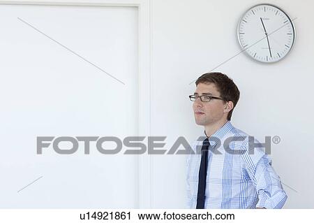 Businessman standing under office clock View Large Photo Image Stock Image - Businessman standing under office clock. Fotosearch