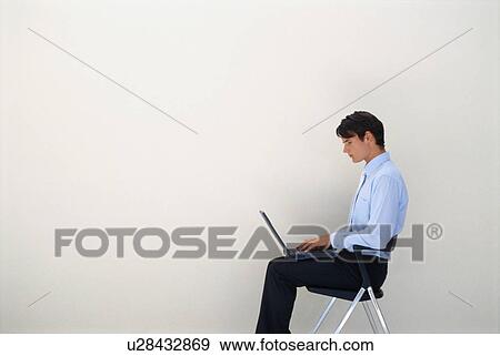Stock Photo - Businessman using laptop in office chair. Fotosearch
