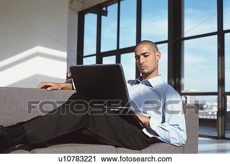Businessman using laptop on couch View Large Photo Image Stock Image - Businessman using laptop on couch. Fotosearch
