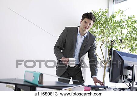 Businessman with cup of coffee at desk View Large Photo Image Stock Image - Businessman with cup of coffee at desk. Fotosearch