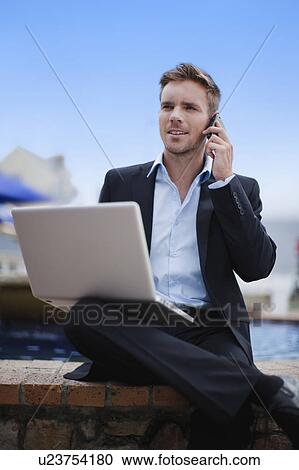 Stock Image - Businessman with laptop on cell phone. Fotosearch