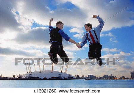 Businessmen jumping against city skyline View Large Photo Image Stock Image - Businessmen jumping against city skyline. Fotosearch