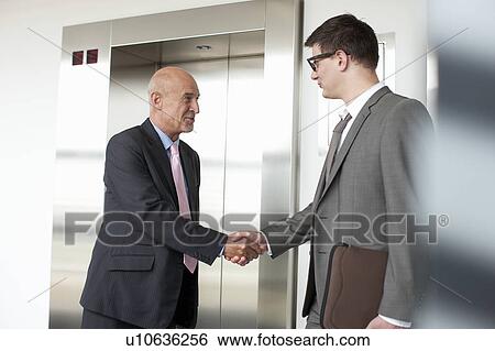 Stock Photograph - Businessmen shaking hands in lobby. Fotosearch