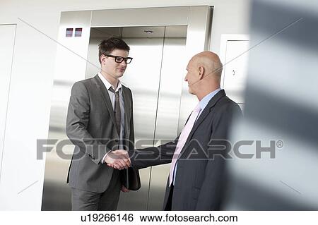Businessmen shaking hands in lobby View Large Photo Image Stock Photograph - Businessmen shaking hands in lobby. Fotosearch