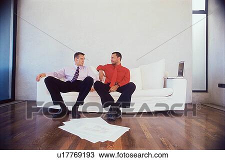 Stock Image - Businessmen talking on couch in office. Fotosearch