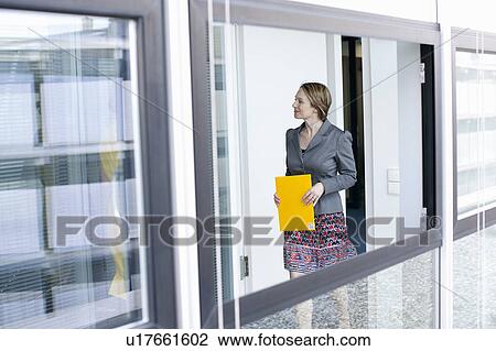 Stock Image - Businesswoman carrying folder in office. Fotosearch
