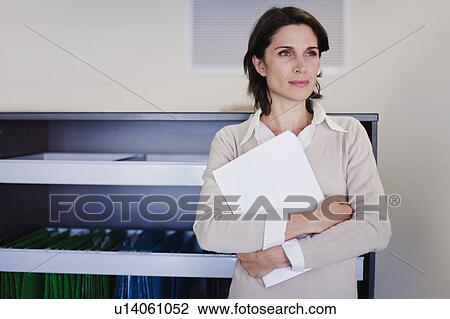 Businesswoman holding papers in office View Large Photo Image Stock Image - Businesswoman holding papers in office. Fotosearch