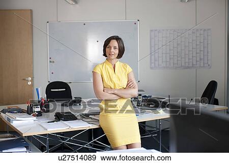Stock Photo - Businesswoman leaning on desk in office. Fotosearch