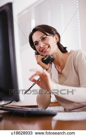 Stock Image - Businesswoman on telephone at computer. Fotosearch