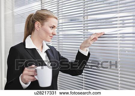 Stock Image - Businesswoman peering out of blinds. Fotosearch