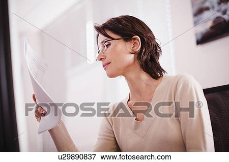 Stock Photo - Businesswoman reading document in office. Fotosearch