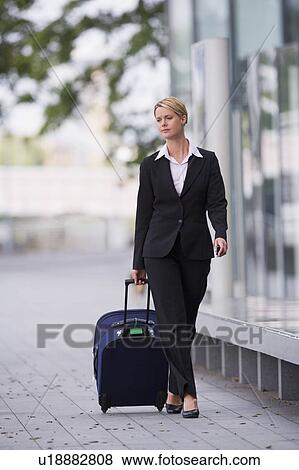 Stock Photo - Businesswoman rolling luggage outdoors. Fotosearch