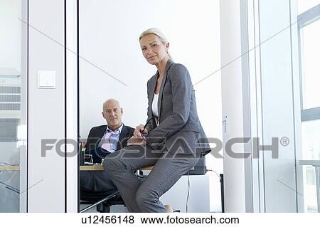 Businesswoman sitting on desk in office View Large Photo Image Stock Photo - Businesswoman sitting on desk in office. Fotosearch