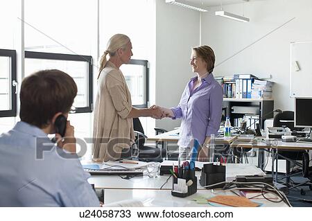 Stock Image - Businesswomen shaking hands in office. Fotosearch