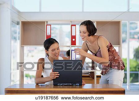 Stock Photograph - Businesswomen using laptop together. Fotosearch