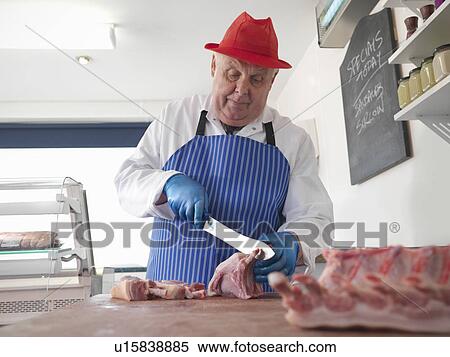 Stock Photography - Butcher carving meat in shop. Fotosearch