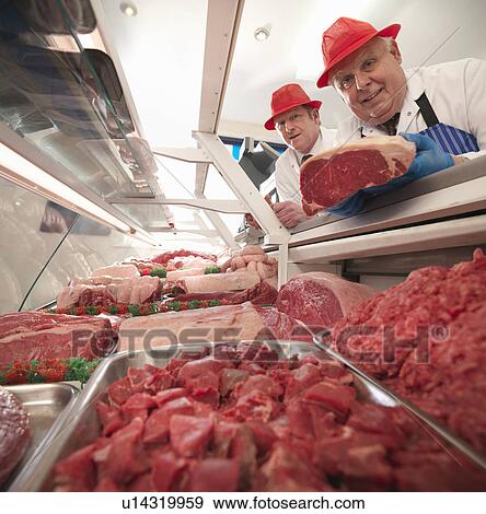 Butcher examining meat in case View Large Photo Image Stock Photo - Butcher examining meat in case. Fotosearch
