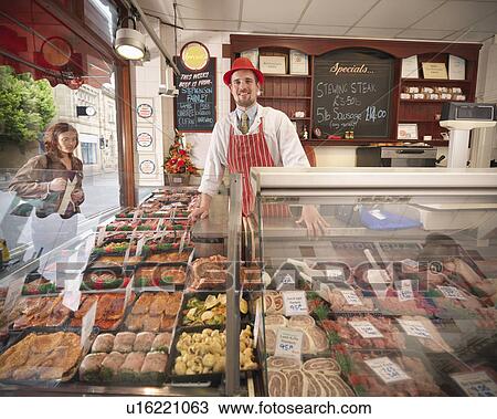 Stock Image - Butcher standing behind counter in shop. Fotosearch