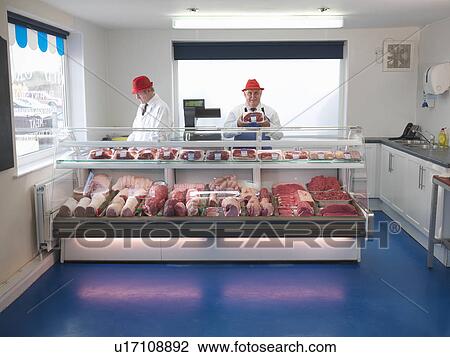 Stock Image - Butcher standing behind meat counter. Fotosearch